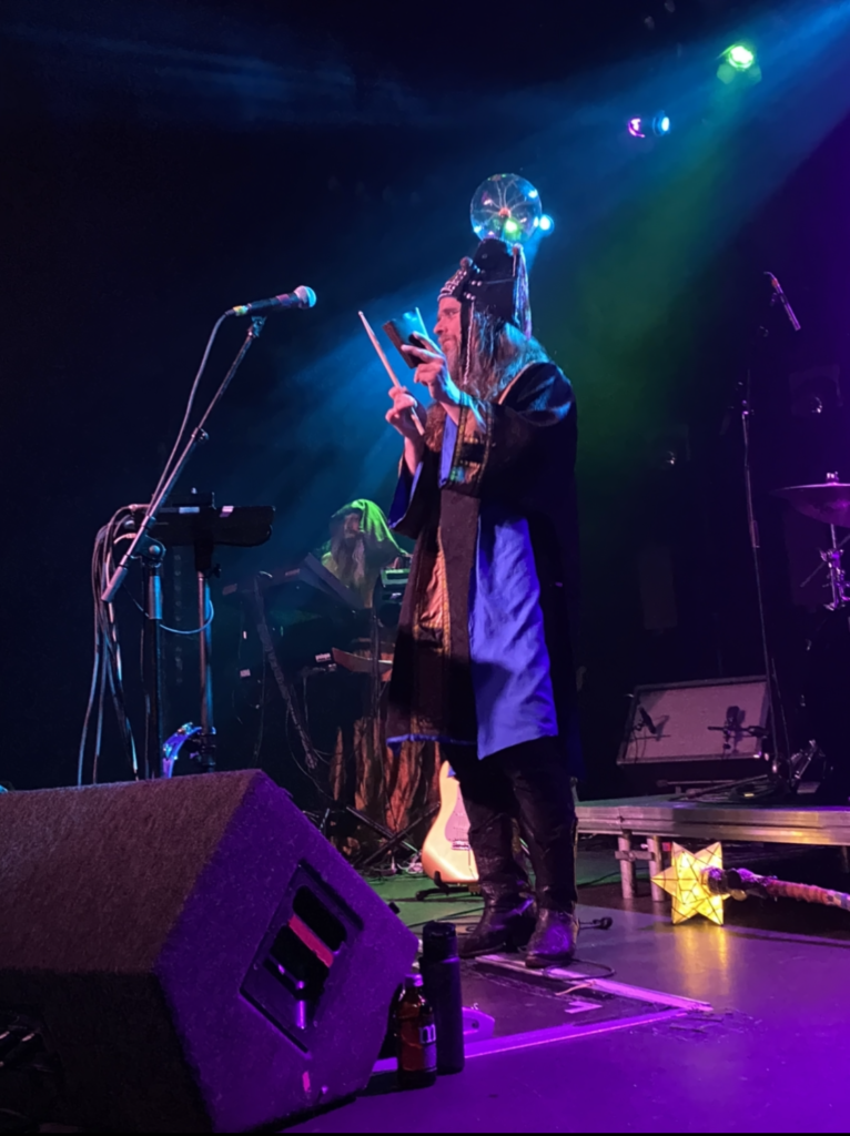 HENGE vocalist playing cowbell with a plasma ball atop his hat which holds his memories