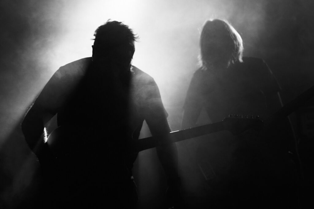 silhouette monochrome image of the two guitarists on a smoke filled stage